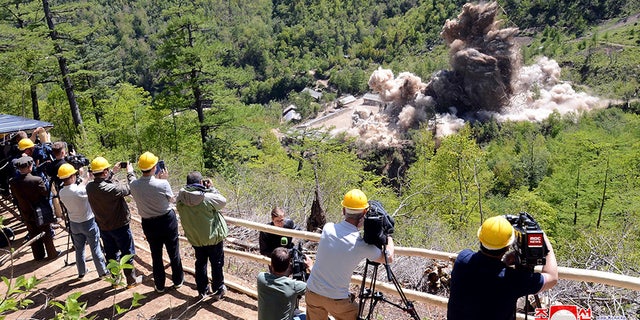 Onlookers wearing hard hats appear to film the demolition of the supposed nuclear test site.