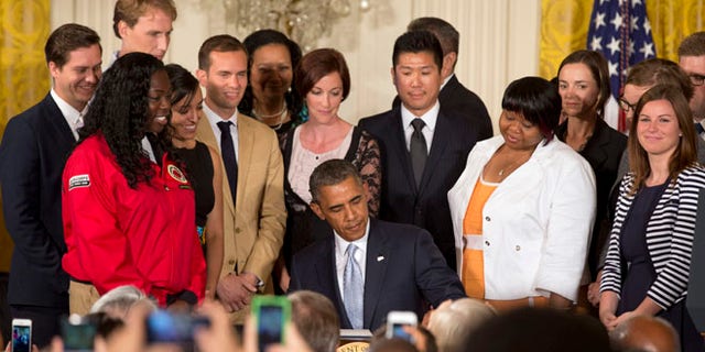 Surrounded by college students, President Barack Obama signs a Presidential Memorandum on reducing the burden of student loan debt, Monday, June 9, 2014, in the East Room of the White House in Washington.