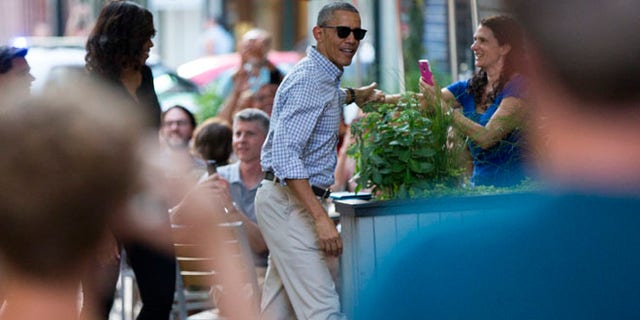 People take photographs as President Barack Obama, center, and first lady Michelle Obama walk into the Oyamel Cocina Mexicana restaurant in Washington for dinner on Saturday, May 28, 2016. (AP Photo/Evan Vucci)