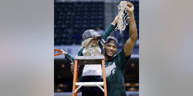 FILE - In this March 16, 2014 file photo, Michigan State forward Adreian Payne, right, hoists the net with Lacey Holsworth, who is battling cancer, after Michigan State defeated Michigan 69-55 in an NCAA college basketball game in the championship of the Big Ten Conference tournament in Indianapolis. The father of 8-year-old Lacey Holsworth, who befriended Michigan State basketball star Adreian Payne says his daughter has died. Matt Holsworth says Lacey Holsworth died at their St. Johns, Mich., home late Tuesday, April 8, 2014 "with her mommy and daddy holding her in their arms." (AP Photo/Michael Conroy, File)