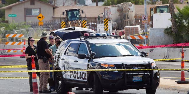 In this Sept. 6, 2015, photo, investigators stand by a Las Vegas Metro Police patrol vehicle after an officer in the vehicle was shot in Las Vegas. A man with a handgun walked up to the SUV as it was waiting at a red light and opened fire, striking one officer in the hand, authorities said. (Steve Marcus/Las Vegas Sun via AP) LAS VEGAS REVIEW-JOURNAL OUT; MANDATORY CREDIT