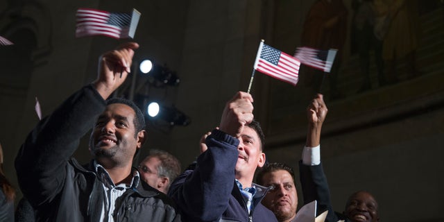 Participants in a naturalization ceremony wave flags after taking the "Oath of Allegiance" at an event attended by President Barack Obama at the National Archive in Washington, Tuesday, Dec. 15, 2015. The president spoke at the National Archives Museum, where 31 immigrants from Iraq, Ethiopia, Uganda and 23 other nations are being sworn in as U.S. citizens. (AP Photo/Evan Vucci)