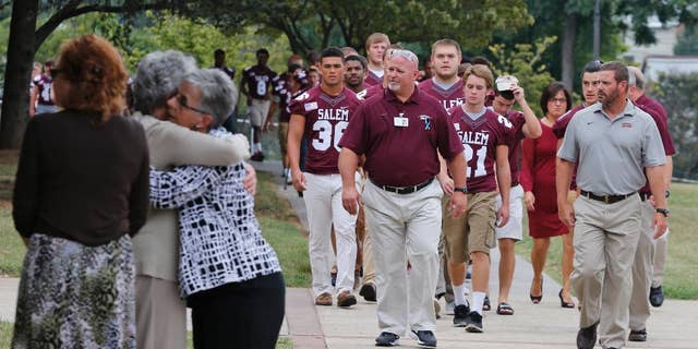 Members of the Salem High school football team arrive to remember alumnus WDBJ-TV cameraman Adam Ward, as mourners hug at Salem High School in Salem, Va., Monday, Aug. 31, 2015. Ward and reporter Alison Parker were gunned down by a former co-worker during a live shot last week. Salem High School opened its doors to the community Monday to commemorate the life of alumnus Ward. (AP Photo/Steve Helber)