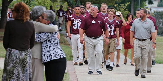 Members of the Salem High school football team arrive to remember alumnus WDBJ-TV cameraman Adam Ward, as mourners hug at Salem High School in Salem, Va., Monday, Aug. 31, 2015. Ward and reporter Alison Parker were gunned down by a former co-worker during a live shot last week. Salem High School opened its doors to the community Monday to commemorate the life of alumnus Ward. (AP Photo/Steve Helber)