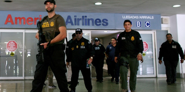 FILE - In this June 6, 2012 file photo, federal agents with the Drug Enforcement Administration escort a handcuffed drug smuggling suspect, at the airport in San Juan, Puerto Rico. U.S. federal agents will start targeting high-level drug traffickers in Puerto Rico after gathering intelligence during a three-month blitz on criminal activity in the U.S. territory, the Department of Homeland Security said Thursday, Sept. 26, 2013 (AP Photo/Ricardo Arduengo)