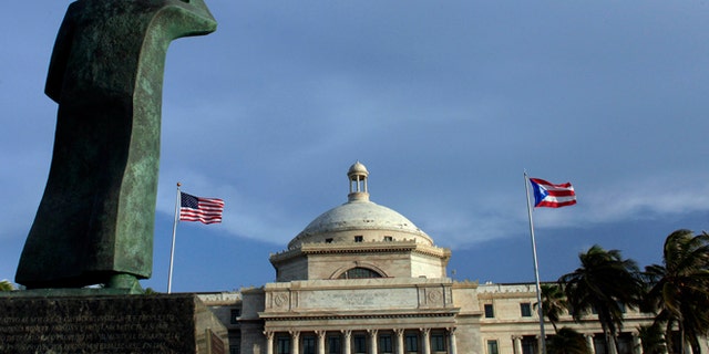 FILE - In this Wednesday, July 29, 2015, file photo, a bronze statue of San Juan Bautista stands in front of Puerto Ricos Capitol as U.S. and Puerto Rican flags fly in San Juan, Puerto Rico. After months of pleading from the government of Puerto Rico, the U.S. Congress agreed on Wednesday, May 18, 2016, to help the territory restructure its massive public debt. (AP Photo/Ricardo Arduengo, File)