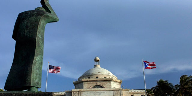 FILE - In this Wednesday, July 29, 2015, file photo, a bronze statue of San Juan Bautista stands in front of Puerto Ricoâs Capitol as U.S. and Puerto Rican flags fly in San Juan, Puerto Rico. After months of pleading from the government of Puerto Rico, the U.S. Congress agreed on Wednesday, May 18, 2016, to help the territory restructure its massive public debt. (AP Photo/Ricardo Arduengo, File)