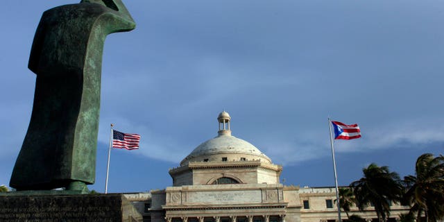 En esta imagen del miércoles 29 de julio de 2015, una estatua de bronce de San Juan bautista ante el capitolio en San Juan, Puerto Rico. Sumido en una crisis económica, el gobierno ha intentado aumentar los ingresos subiendo el impuesto sobre la venta al 11,5%, más alto que en cualquier estado de EEUU, y cerrado oficinas gubernamentales. (AP Foto/Ricardo Arduengo)