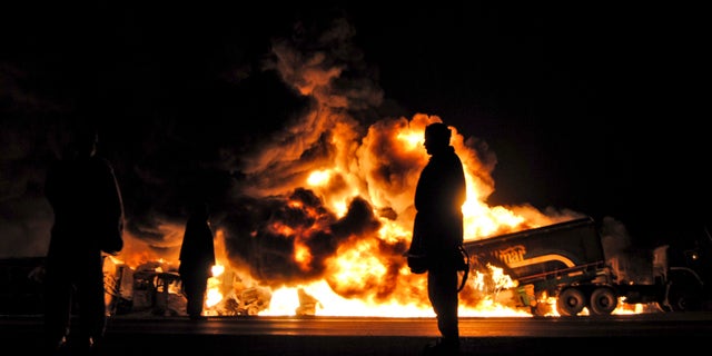 Pakistanis gather by burning oil tankers after gunmen attacked a terminal in Dera Murad Jamali southwest Pakistan, early Saturday, Jan. 15, 2011. A government official says gunmen in Pakistan's southwest have set ablaze 14 tankers carrying fuel for U.S. and NATO troops in Afghanistan. A driver also was wounded during the Saturday attack.