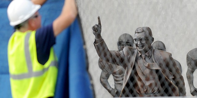 July 22, 2012: Worker hangs a blue tarp over the fence that was installed around the Joe Paterno statue as crews worked to remove the statue in State College, Pa.