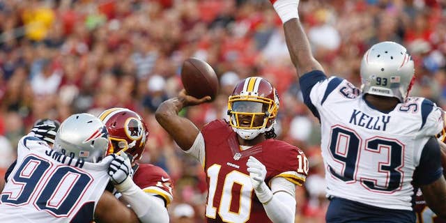 Washington Redskins quarterback Robert Griffin III passes between New England Patriots defensive end Will Smith (90) and defensive tackle Tommy Kelly (93) during the first half of an NFL football preseason game in Landover, Md., Thursday, Aug. 7, 2014. (AP Photo/Alex Brandon)