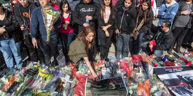 A fan places a poster during a memorial rally and car cruise in Valencia, Calif., Sunday, Dec. 8, 2013 to remember actor Paul Walker and his friend Roger Rodas, who died in a fiery car crash last Saturday. (AP Photo/Ringo H.W. Chiu)