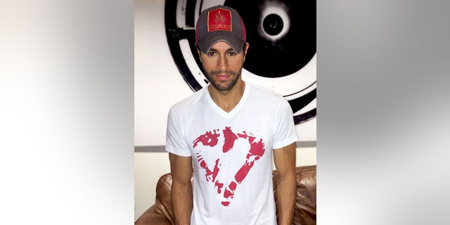 In this Sept. 30, 2015 photo provided by Enrique Iglesias, Iglesias wears his new heart T-shirt in Miami. Following an accident with a drone that led to reconstructive hand surgery, Iglesias is giving a helping hand to children dealing with emergencies. Save the Children said Monday, Oct. 26, 2015, that Iglesias is working with the organization to sell white T-shirts with a red heart at its center - mirroring how Iglesias shirt looked after he cut his fingers at a concert and wiped the blood on his shirt. (Francis Ramsden/Enrique Iglesias via AP)
