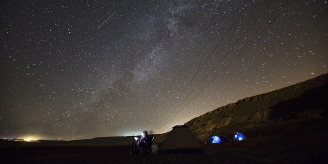 A meteor streaks across the sky in the early morning as people watching during the Perseid meteor shower in Ramon Carter near the town of Mitzpe Ramon, southern Israel, Aug.13, 2015.