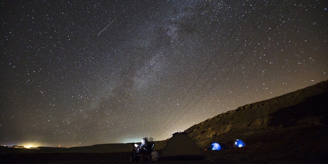 A meteor streaks across the sky in the early morning as people watching during the Perseid meteor shower in Ramon Carter near the town of Mitzpe Ramon, southern Israel, Aug.13, 2015.