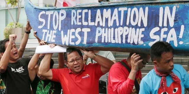 In this July 3, 2015, file photo, protesters carry a boat painted with slogans during a rally outside the Chinese Consulate at the financial district of Makati city, east of Manila, Philippines, to protest China's reclamations of disputed islands off South China Sea. China is standing pat on its decision to reject arbitration by an international tribunal that will begin formal hearings this week to resolve a long-seething feud with the Philippines over the South China Sea, Beijing's ambassador to Manila said Monday, July 6, 2015. (AP Photo/Bullit Marquez)