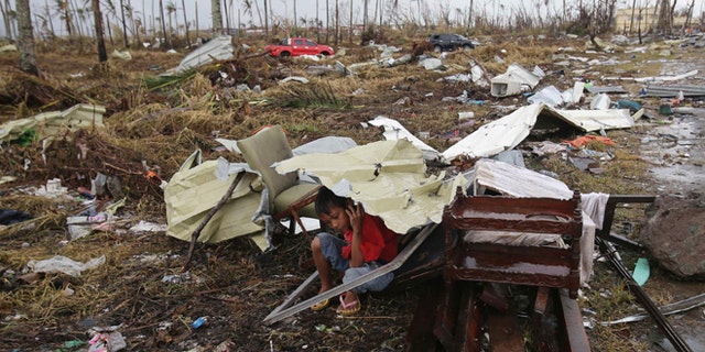 A young survivor uses the remains of some parts of a house to shield him from rain in Tacloban city, Leyte province, central Philippines on Tuesday, Nov. 12, 2013.