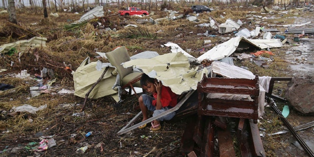 A young survivor uses the remains of some parts of a house to shield him from rain in Tacloban city, Leyte province, central Philippines on Tuesday, Nov. 12, 2013.