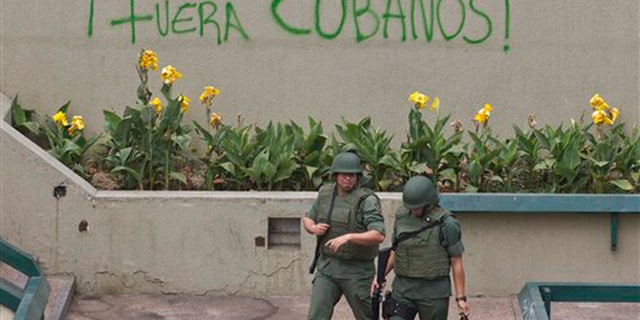 Bolivarian National Guard officers patrol Plaza Altamira after taking control of it, in Caracas, Venezuela, Monday, March 17, 2014. Government security forces took control of a Caracas plaza and surrounding neighborhoods Monday morning that had become the center of student-led protests. The graffiti on the wall reads in Spanish "Cubans Out!". Clusters of National Guardsmen were a visible presence not only on Plaza Altamira, but along the principal streets extending from it in the municipality of Chacao.