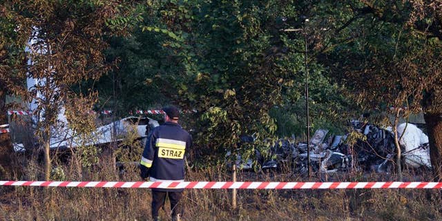 A firefighter officer examines the crash site of a plane near the village of Topolow in Poland, Saturday, July 5, 2014. The small Piper Navajo aircraft carrying parachutists crashed and burst into flames shortly after takeoff, killing several people and injuring at least one. (AP Photo)