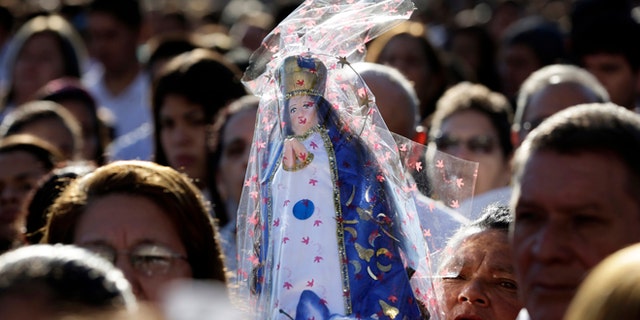 FILE - In this June 7, 2015, file photo, a woman carries a Caacupe virgin replica during Corpus Christi mass in Caacupe city, Paraguay. Hundreds of thousands turn out every December to worship before the little wooden statue of the Virgin Mary, who wears a crown over her long hair, with a billowing white robe and a blue cloak. (AP Photo/Jorge Saenz, File)