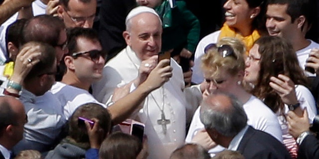 Pope Francis poses for pictures with faithful at the end of a Palm Sunday service in St. Peter's Square, at the Vatican, Sunday, April 13, 2014. Pope Francis, marking Palm Sunday in a packed St. Peter's Square, ignored his prepared homily and spoke entirely off-the-cuff in a remarkable departure from practice. Later, he hopped off his popemobile to pose for "selfies" with young people in the crowd. In his homily, Francis called on people, himself included, to look into their own hearts to see how they are living their lives. (AP Photo/Gregorio Borgia)