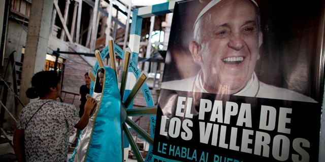 A woman touches a religious figure beside a banner of Pope Francis reading in Spanish, "The Pope of the people of the slum" as she attends a mass in his honor at the 1-11-14 slum's church in Buenos Aires, Argentina, Thursday, March 13, 2014. On the day of the first anniversary of the Pope's election, people from the 1-11-14 slum gather at their church to watch an interview that Pope Francis gave recently from his residence at the Vatican to FM Bajo Flores, a community radio station that broadcasts from the slum. (AP Photo/Natacha Pisarenko)