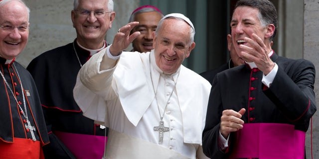 FILE – Pope Francis, flanked by rector of the Pontifical North American College James F. Checchio, right, Cardinal Marc Ouellet, left, and President of the United States Conference of Catholic Bishops Joseph Edward Kurtz, greets the faithful as he leaves Rome's Pontifical North American College, Saturday, May 2, 2015. Pope Francis has praised the "holiness" of an 18th-century Franciscan missionary hell make a saint when he visits the United States this fall but whom Native Americans in California contend brutally converted indigenous people to Christianity. Francis on Saturday praised the accomplishments and qualities of Rev. Junipero Serra during a homily at a Rome seminary training future priests from North America. (AP Photo/Andrew Medichini)