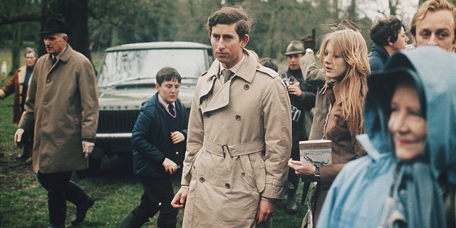 Prince Charles, wearing a belted trench coat, stands with a girlfriend at an outdoor horse event circa 1970. A Range Rover Classic car can be seen in the background. (Photo by Rolls Press/Popperfoto/Getty Images)