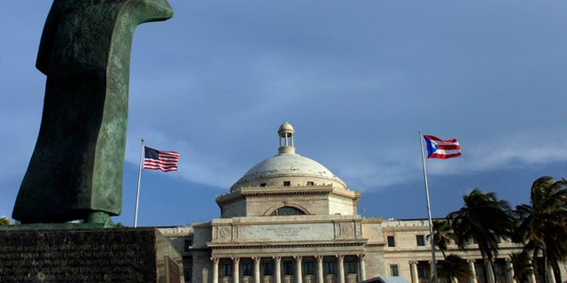 FILE - In this Wednesday, July 29, 2015, file photo, a bronze statue of San Juan Bautista stands in front of Puerto Ricoâs Capitol as U.S. and Puerto Rican flags fly in San Juan, Puerto Rico. After months of pleading from the government of Puerto Rico, the U.S. Congress agreed on Wednesday, May 18, 2016, to help the territory restructure its massive public debt. (AP Photo/Ricardo Arduengo, File)
