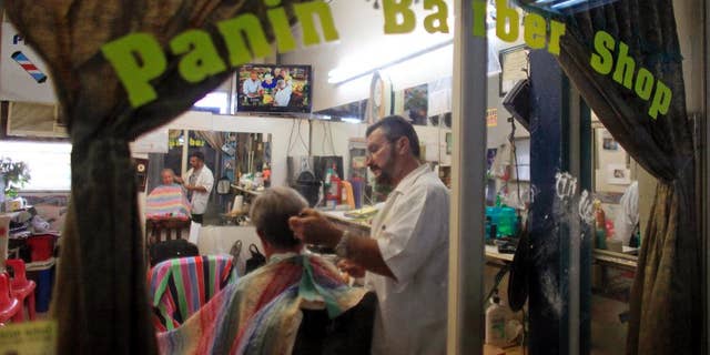 In this Sept. 2, 2015 photo, Francisco Gonzalez gives a haircut to a customer at his barbershop in Lares, Puerto Rico. Despite the economic downturn, some business owners are determined to stick it out in Lares. (AP Photo/Ricardo Arduengo)