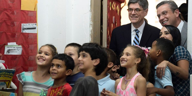 U.S. Treasury Secretary Jacob Lew, top, second from right, poses for photos with students as he takes a classroom tour with Puerto Rico Governor Alejandro Garcia Padilla, top right, at the Eleanor Roosevelt Elementary School in San Juan, Puerto Rico, Monday, May 9, 2016. Lew hoped to jump-start congressional efforts to aid debt-stricken Puerto Rico, traveling to the U.S. territory on Monday and focusing on basic services in jeopardy at public hospitals and schools. (AP Photo/Carlos Giusti)