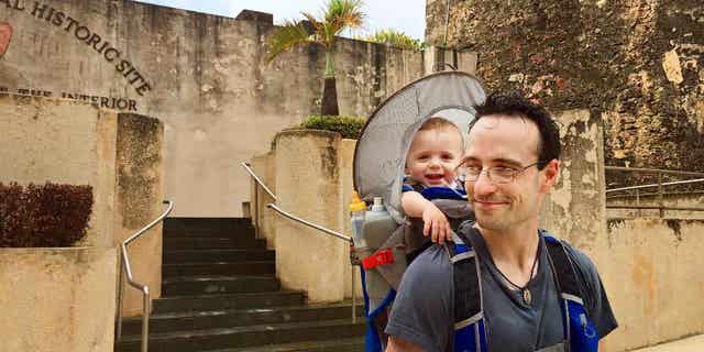 In this May 22, 2015 photo, Elijah Van Benschoten carries his 17-month-old son Hunt Van Benschoten while visiting Castillo de San Cristobal in San Juan, Puerto Rico. No matter how experienced a traveler you are, an overseas trip taken with a baby or toddler requires changes in planning, expectations and itineraries. (Amber Hunt via AP)