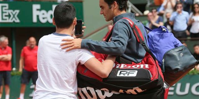 A boy who climbed down from the stands takes a selfie with Switzerland's Roger Federer in the first round match of the French Open tennis tournament in Paris, France, Sunday, May 24, 2015. (AP Photo/David Vincent)