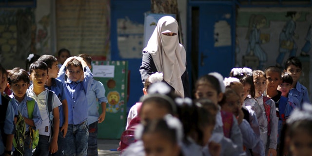 September 22, 2015: A veiled Palestinian teacher stands next to children as they queue at a United Nations Relief and Work Agency (UNRWA)-run school in Gaza. A recent investigation by the Center for Near East Policy Research found that many of the schools are using texts that are authored by the Palestinian Ministry of Education and its contents not fail to recognize the state of Israel.