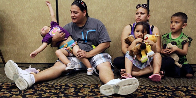 FILE - In this Wednesday, May 15, 2013 file photo, Elijah Bearsheart, left, holds his daughter, Keanala, 1, as he sits with his family, Kehala Diserly, Kiari Diserly, 3, and Yamni Pederson, 5, as they listen to testimony during the Indian Child Welfare Act summit in Rapid City, S.D. A new report on child well-being, measured by state and race, has turned an unflattering spotlight on some places not used to being at the bottom of such lists, including Wisconsin, with a worst-in-the-nation ranking for its black children, and South Dakota, with abysmal results for its American Indian youth. The report was released Tuesday, April 1, 2014 by the Annie E. Casey Foundation. (AP Photo/Rapid City Journal, Benjamin Brayfield)