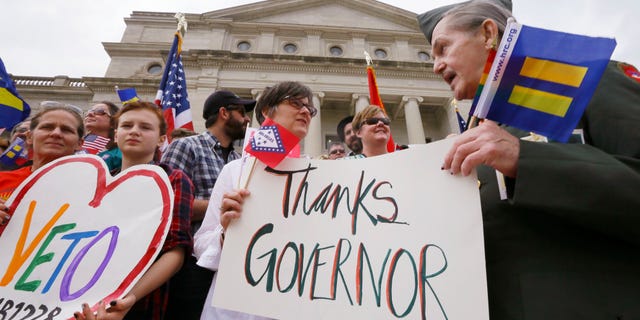 Kristen Hooper, center, and Robert Loyd, right, hold a sign on the steps of the Arkansas state Capitol thanking Arkansas Gov. Asa Hutchinson for calling for changes to a religious objection measure in Little Rock, Ark., Wednesday, April 1, 2015. The measure faced a backlash from businesses and gay rights groups. (AP Photo/Danny Johnston)