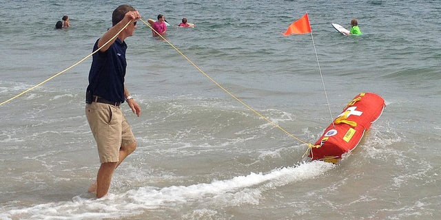 Aug, 8, 2012: Misquamicut, R.I., Fire Chief Louis Misto, left, holds a line attached to the EMILY remote-control lifesaving device as it propels itself in the water and away from the shore at Old Town Beach, in Westerly, R.I.