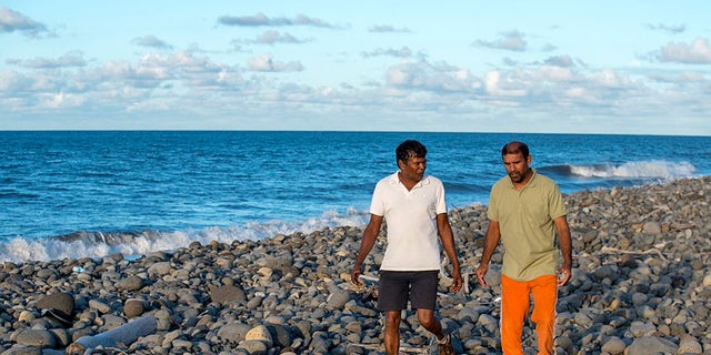 July 30, 2015 - Johnny Begue (R), who found plane debris Wednesday on this beach in Saint-Andre, on the French Indian Ocean island of La Reunion, walks with his friend Andre Tevane. Begue found a flaperon, which help pilots control an aircraft in flight, on Wednesday.  French authorities are studying the piece to determine whether it came from Malaysia Airlines Flight MH370.