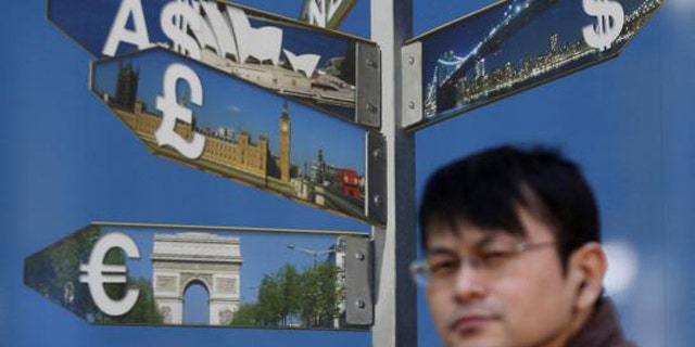 October 28, 2014: A man walks past various currency signs, including the dollar, Australian dollar, pound sterling and euro, outside a brokerage in Tokyo (Reuters/Yuya Shino)