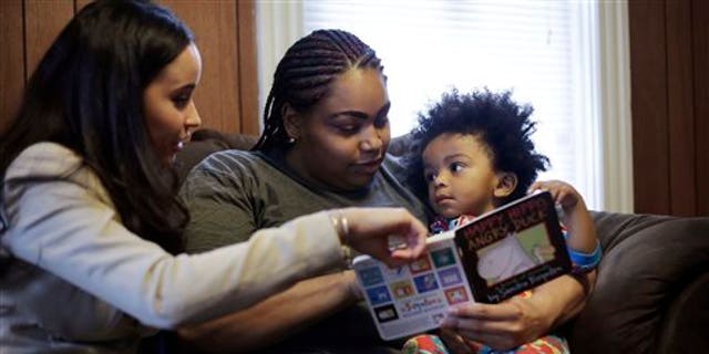 In this Feb. 3, 2014 photo, caseworker and home visitor Stephanie Taveras, left, reads a book with Ashley Cox, center, and Cox's 16-month-old son Jaiden, right, at the family's home in Providence, R.I. The city has begun an effort to boost language skills for children from low-income families by equipping them with audio recorders that count every word they hear. During home visits, social workers go over the word counts with parents and suggest tips to boost the childs language skills. (AP Photo/Steven Senne)