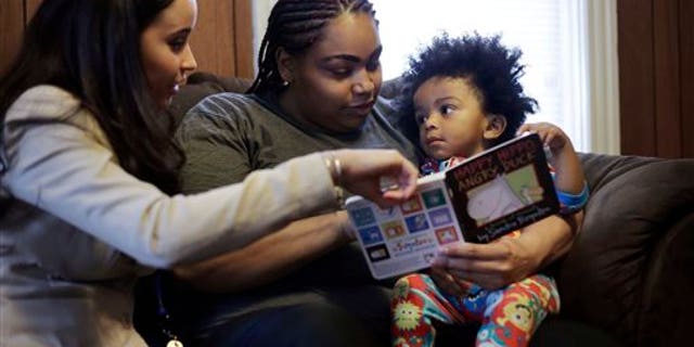 In this Feb. 3, 2014 photo, caseworker and home visitor Stephanie Taveras, left, reads a book with Ashley Cox, center, and Cox's 16-month-old son Jaiden, right, at the family's home in Providence, R.I. The city has begun an effort to boost language skills for children from low-income families by equipping them with audio recorders that count every word they hear. During home visits, social workers go over the word counts with parents and suggest tips to boost the childs language skills. (AP Photo/Steven Senne)