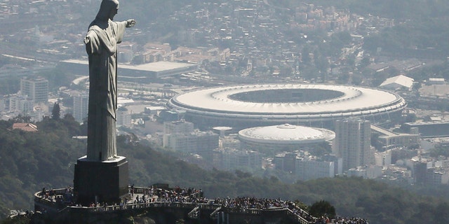 RIO DE JANEIRO, BRAZIL - JULY 04: Visitors gather beneath the Christ the Redeemer statue as Maracana stadium, site of the Olympic opening ceremonies, stands in the background on July 4, 2016 in Rio de Janeiro, Brazil. July 5 marks the one-month mark to the beginning of the Rio 2016 Olympic Games with an economic crisis, political turmoil and Zika virus fears roiling the country. (Photo by Mario Tama/Getty Images)