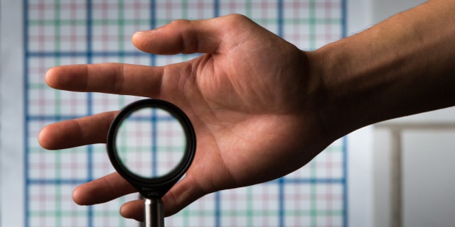 A multidirectional `perfect paraxial' cloak using 4 lenses. For a continuous range of viewing angles, the hand remains cloaked, and the grids seen through the device match the background on the wall (about 2 m away), in color, spacing, shifts, and magnification. The edges of the optics can be seen since this is a small-angle ('paraxial') cloak, but this can be reduced by using large optics and for distant viewing; also the center of the device must not be blocked. // an optical cloaking configuration designed by University of Rochester professor of physics John C. Howell and Ph.D. student Joseph Choi is pictured in Bausch & Lomb Hall September 11, 2014. // photo by J. Adam Fenster / University of Rochester