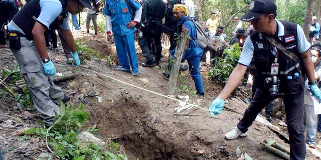 May 2, 2015: Thai police officials measure a shallow grave in Padang Besar, Songkhla province, southern Thailand. (AP Photo/Sumeth Panpetch, File)