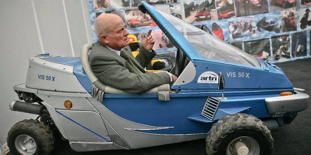 In a photo taken on March 24, 2009, Justin Capra, a Romanian inventor who claimed he beat the Americans to make the world’s first jet-pack, seen on photo wall behind top left, gestures sitting in a fuel efficient vehicle he designed at an inventions fair in Cluj, Romania. Capra, who in 1956 invented the “flying rucksack,” a personal flying machine, very similar, according to him to the one built in 1962 in the U.S. by Bell Aircraft Corp., has died Monday, Jan. 19, 2015, aged 81.(AP Photo/Mircea Rosca)