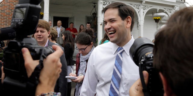 In this April 17, 2015 photo, Republican presidential candidate, Sen. Marco Rubio, R-Fla., laughs as he is surrounded by media at a campaign house party in Manchester, N.H. Devoted political allies for more than a decade, the alliance between former Florida Gov. Jeb Bush and Rubio is beginning to splinter as the one-time mentor and his political protégé face off in the race for the Republican presidential nomination. (AP Photo/Elise Amendola)