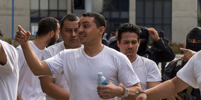 In this Tuesday, Aug. 2, 2016 photo, handcuffed to another prisoner, Marvin Quintanilla Ramos, center, an evangelical pastor accused by El Salvador Police to be the financier of Mara Salvatrucha gang, is walked out after a court hearing in San Salvador, El Salvador. Prosecutors allege that Ramos used his pastoral credentials to access prisons so he could conspire with jailed leaders of the gang. Religion, they say, was a facade to mask his real work: helping run Mara Salvatruchas street operations and directing its finances at a key moment when gangs are facing a tough crackdown by the government and are moving to diversify their criminal operations and become more corporate in makeup and structure. (AP Photo/Salvador Melendez)