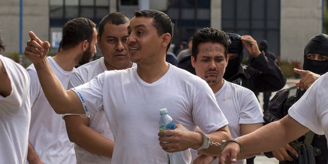 In this Tuesday, Aug. 2, 2016 photo, handcuffed to another prisoner, Marvin Quintanilla Ramos, center, an evangelical pastor accused by El Salvador Police to be the financier of Mara Salvatrucha gang, is walked out after a court hearing in San Salvador, El Salvador. Prosecutors allege that Ramos used his pastoral credentials to access prisons so he could conspire with jailed leaders of the gang. Religion, they say, was a facade to mask his real work: helping run Mara Salvatruchas street operations and directing its finances at a key moment when gangs are facing a tough crackdown by the government and are moving to diversify their criminal operations and become more corporate in makeup and structure. (AP Photo/Salvador Melendez)