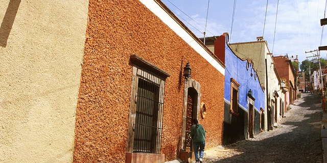 Mexico, San Miguel De Allende, Person Standing In Front Of A Doorway On A Cobblestone Roadway. (Photo by Education Images/UIG via Getty Images)